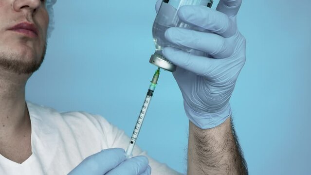 In slow motion Doctor in a gown in sterile mittens, Gathering medicine from a medical jar into a syringe. Treatment liquid medicine in a syringe