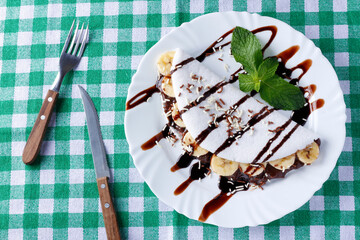 homemade tapioca or beiju stuffed with banana and chocolate on white plate over rustic wooden table