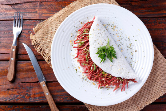 Tapioca or beiju stuffed with dried meat, jerked beef on a rustic wooden table. Typical Brazilian food