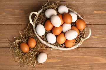 Wicker basket with Easter eggs and hay on brown wooden background