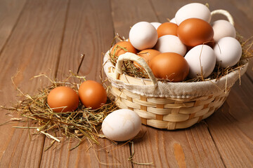 Wicker basket with Easter eggs and hay on brown wooden background