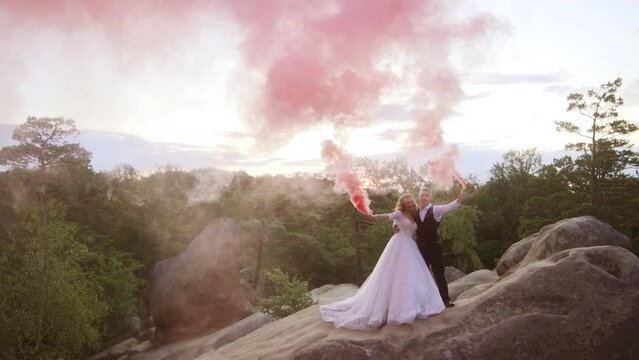 Happy bride and groom waving color red smoke bomb in slow motion on a rock