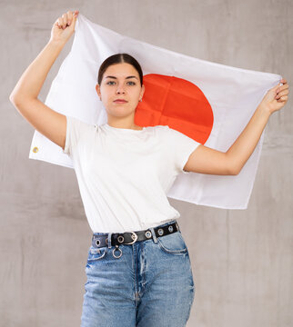 Calm cheerleader girl holds Japan flag in her hands. Isolated on gray background