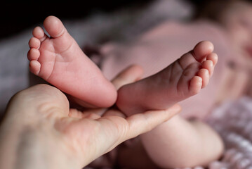 Baby's feet are in the mother's hand. Cozy morning bedtime at home. Naked baby's feet of a baby girl in the folds. Lovely infant foot. Bare feet of a cute newborn baby girl.