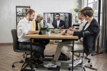Team of four focused multiethnical businesspeople looking at screen, having video conference in modern office, with their colleague explaining some financial charts during telemeeting.