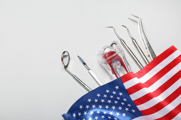 Dental tools with plastic tooth and USA flag on light background, closeup