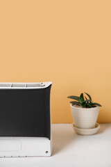 Air purifier and succulent on table near yellow wall, closeup