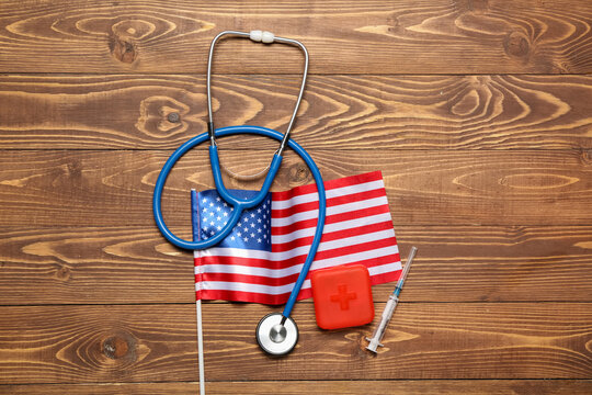 Stethoscope with pill container, syringe and USA flag on wooden background