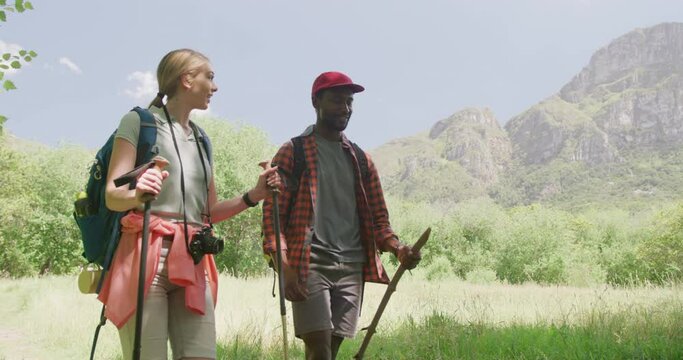 Happy diverse couple hiking with backpacks in park, slow motion