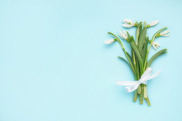 Fototapeta na wymiar Bouquet of beautiful snowdrops tied with ribbon on blue background