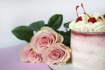 Fototapeta na wymiar Pink Cake decorated with frosting and maraschino cherries. Half of the cake and fresh roses in the center, close up.
