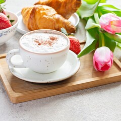Happy mother's day, beautiful breakfast, lunch with cup of coffee (cappuccino) fresh croissants, strawberries on tray, bouquet of tulips as gift. Festive concept. Spring holiday, family relations.