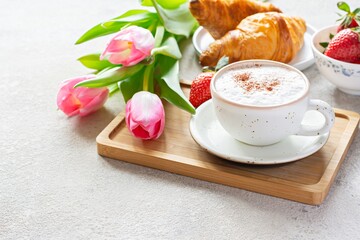 Fototapeta na wymiar Happy mother's day, beautiful breakfast, lunch with cup of coffee (cappuccino) fresh croissants, strawberries on tray, bouquet of tulips as gift. Festive concept. Spring holiday, family relations.