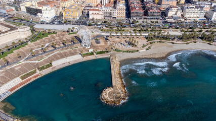 Panoramic view of the city of Civitavecchia with the adjoining tourist port and Forte Michelangelo. Emerald sea and view with tropical palm trees. Ferris wheel and cloudy sky.