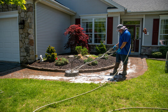 Handyman Using A Circular Power Washer To Clean A Brick Walkway In Front Of A House