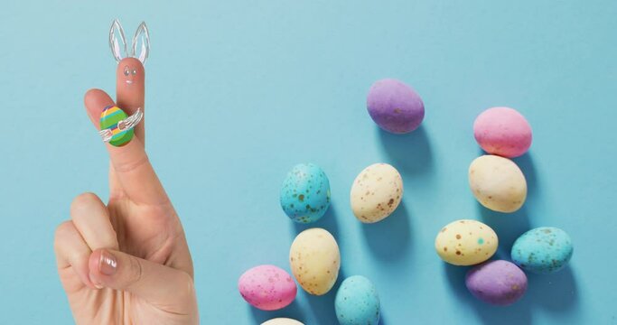Animation of hand with easter decorations and easter eggs over blue background