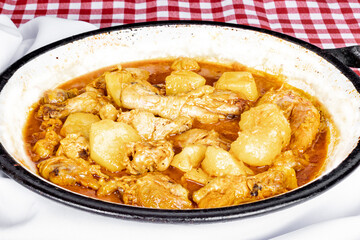 homemade chicken stew with tomato, onion and potato on checkered tablecloth.