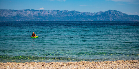 relaxed girl in a bikini floating on a strawberry shaped mattress in adriatic sea, croatia; leisure...