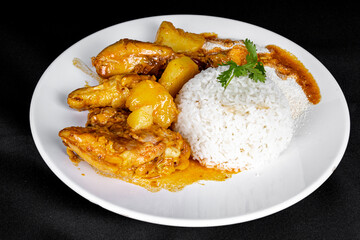 homemade chicken stew with tomato, onion and potato on black fabric table and plate with rice