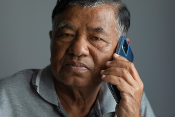 Unhappy senior man thinking while using smartphone in studio. old man with sad face