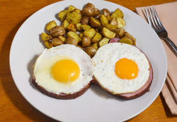 two fried eggs on ham  with a side of home fries,