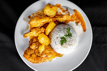 homemade chicken stew with tomato, onion and potato on black fabric table and plate with rice