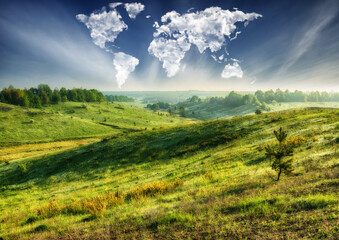 clouds in the form of a world map over a green field. Travel and landscape concept. hilly field