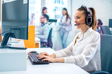 Colorful photo of female IT sector operator with headset talking on microphone during online support call and using computer at office. - obrazy, fototapety, plakaty