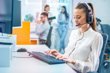 Vibrant color photo of female agent with headset using computer in office.