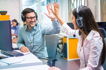 Customer support representative operators giving high five to each other celebrating successful...