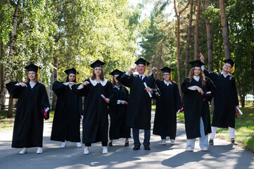 Group of graduates in robes dancing outdoors. Elderly student.