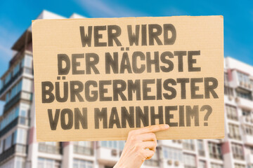 The phrase " Who's the next mayor of Mannheim? " on a banner in men's hands blurred the background. Election. City management. Politics. Urban. Voter. Candidate