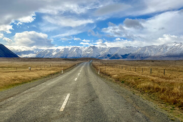 Fototapeta na wymiar The long country road winding its way through the grass and tussock valley being grazed by farmers on the way to the Ben Ohau snow capped mountain range