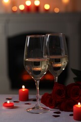 Glasses of white wine, rose flowers and burning candles on grey table indoors. Romantic atmosphere