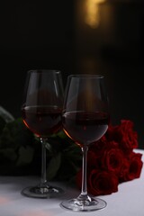 Glasses of red wine and rose flowers on white table. Romantic atmosphere