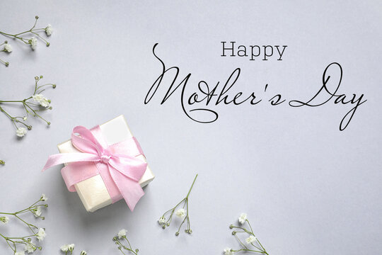 Happy Mother's Day. Greeting card with gift box and beautiful flowers on light grey background, flat lay
