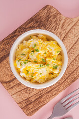 Scrambled eggs on bowl, pink background, top view, vertical
