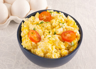 Scrambled eggs with tomatoes on a bowl, white table