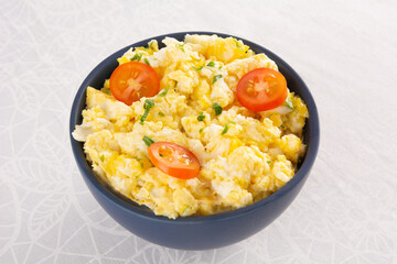 Scrambled eggs with tomatoes on a bowl, white table