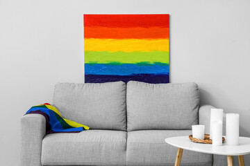 Sofa with LGBT flag, painting and candles on table near light wall