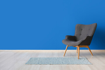 Stylish grey armchair and rug near blue wall