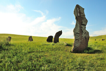 A group of ancient burial stones in a picturesque valley with dense green grass under a clear summer sky.