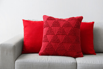Stylish red pillows on comfortable sofa near light wall, closeup