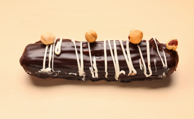 Delicious chocolate eclair with hazelnuts on beige background