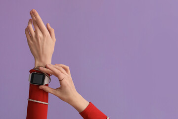 Woman with smartwatch and bracelets on lilac background