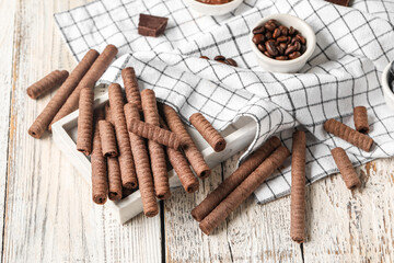 Delicious chocolate wafer rolls and coffee beans on white wooden background