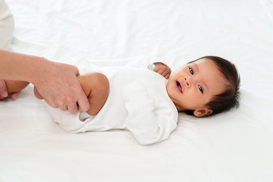 mother's hands holding baby legs and doing some playful exercises on bed