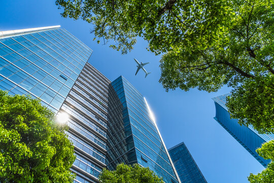 Tall City Buildings And A Plane Flying Overhead.