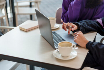 Close-up view of two people using a laptop at a coffee shop.