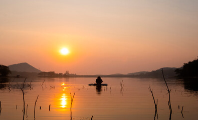 Fishermen's boats gently glide on the reservoir's calm waters during sunrise as they cast their...